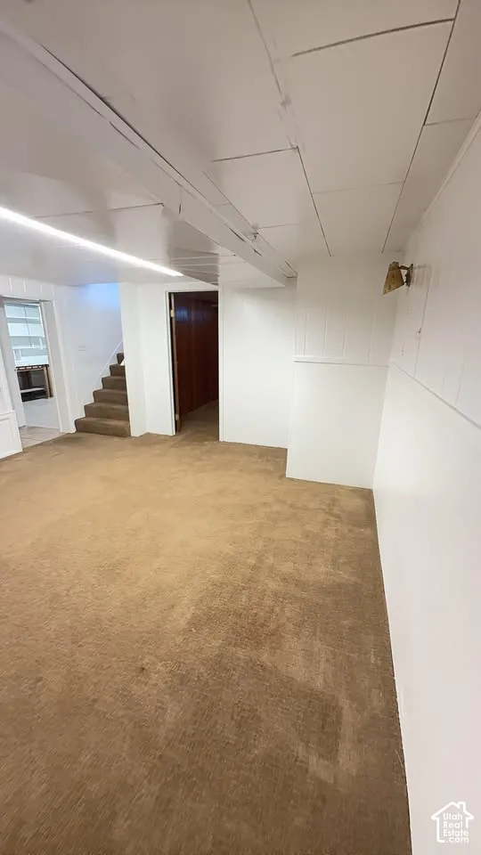 Neutral-toned carpeting, white paneling, integrated linear lighting, and stairwell access