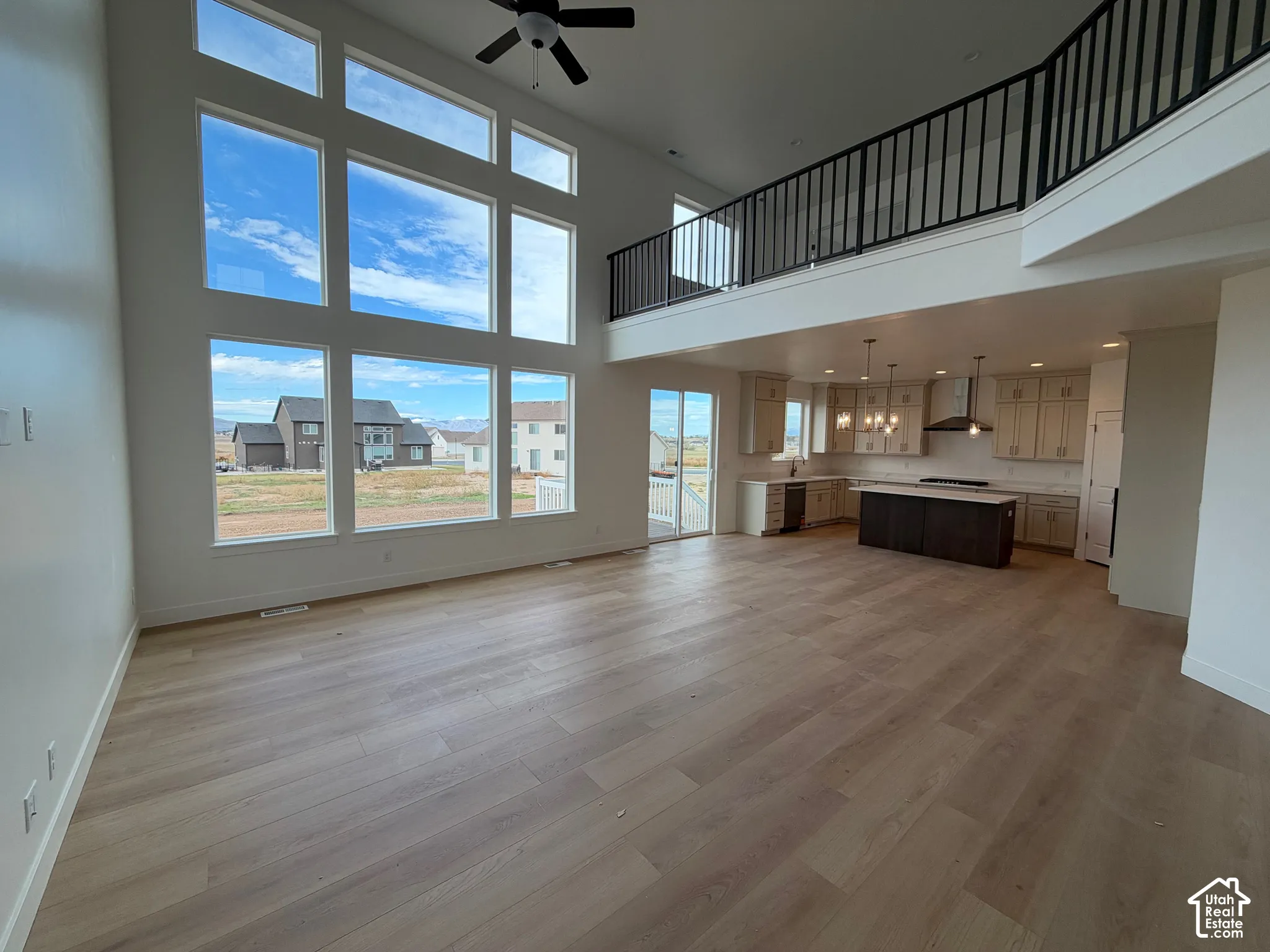 Expansive double-height windows, wood-finish flooring, custom cabinetry, a central kitchen island, and a metal-railing mezzanine