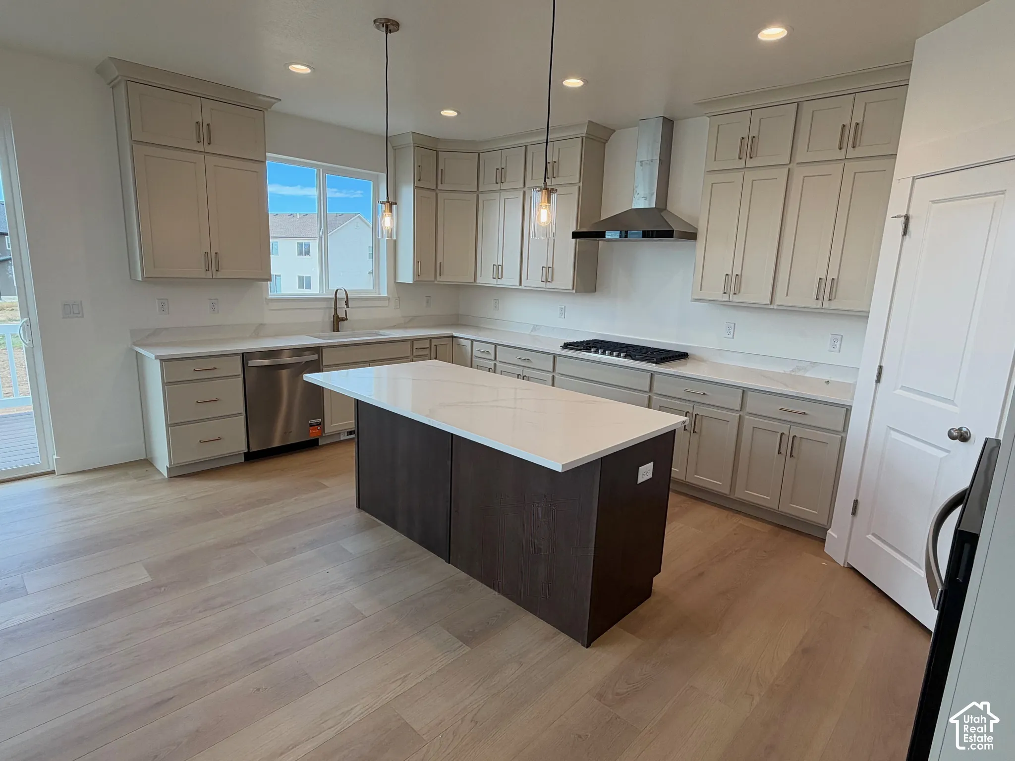 Kitchen featuring light-toned cabinetry, a contrasting dark central island, quartz countertops, stainless steel appliances, and wood-finish flooring