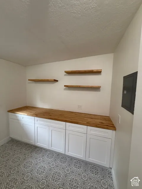 White cabinetry with shaker-style doors, natural wood-finish countertop, patterned tile flooring, and three wall-mounted wood floating shelves