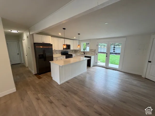 Kitchen featuring white cabinetry, an island with stone countertop, wood-finish flooring, glass-panel double doors, and a tile backsplash