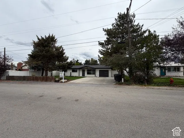 Single-story exterior featuring white masonry siding, dark trim accents, a concrete driveway, an attached garage, and mature landscaping