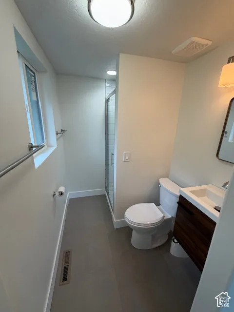 Bathroom featuring a wood-finish vanity with an integrated sink, large-format tile flooring, a glass-enclosed shower, and wall-mounted light fixtures