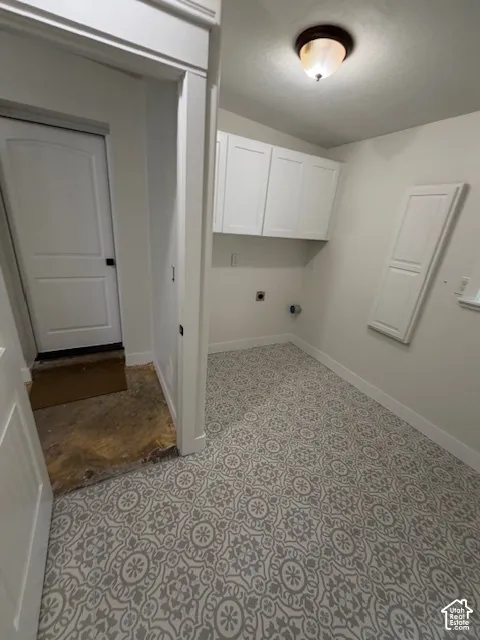Laundry area featuring patterned tile flooring, white wall-mounted cabinetry, a flush-mount ceiling light fixture, and a white paneled door