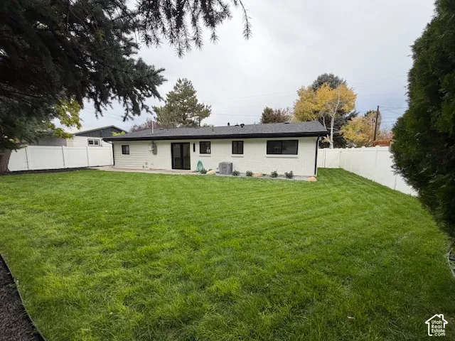 Expansive backyard featuring a manicured lawn, white vinyl perimeter fencing, and mature trees