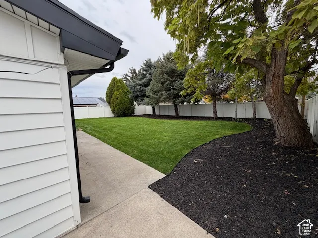 Rear yard featuring a concrete patio, manicured lawn, mulched garden beds, and white vinyl privacy fencing