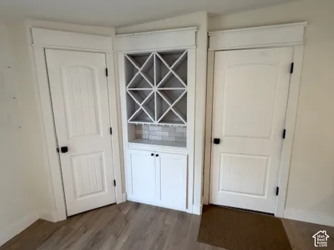 Built-in cabinetry featuring a diamond-grid wine rack, lower storage cabinets, light-toned tile backsplash, and two-panel interior doors with matte black hardware atop wood-finish flooring