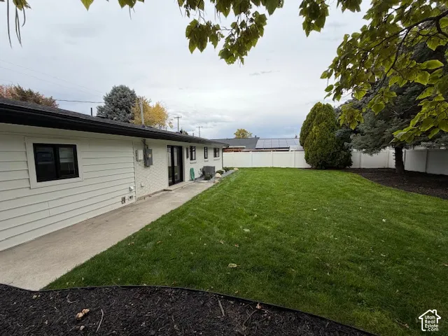 Backyard featuring a concrete patio, a grass lawn, white vinyl perimeter fencing, and mature trees