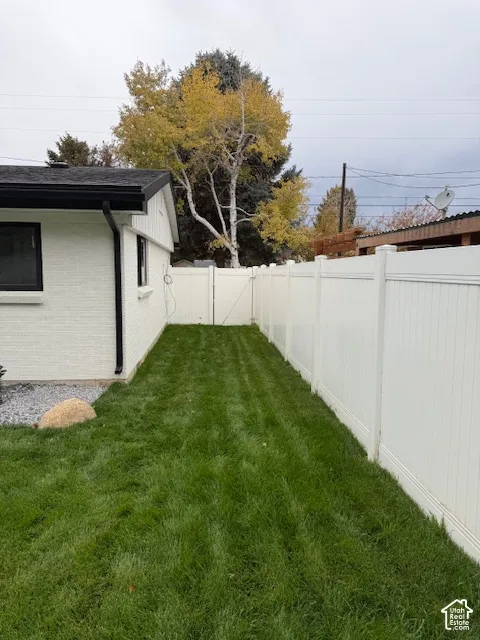 Side yard featuring a lawn, white vinyl fencing, and a painted brick exterior with black trim