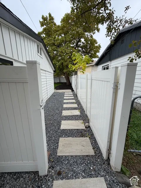 Side exterior pathway featuring white vinyl privacy fencing, stone paver steps, and crushed stone ground cover