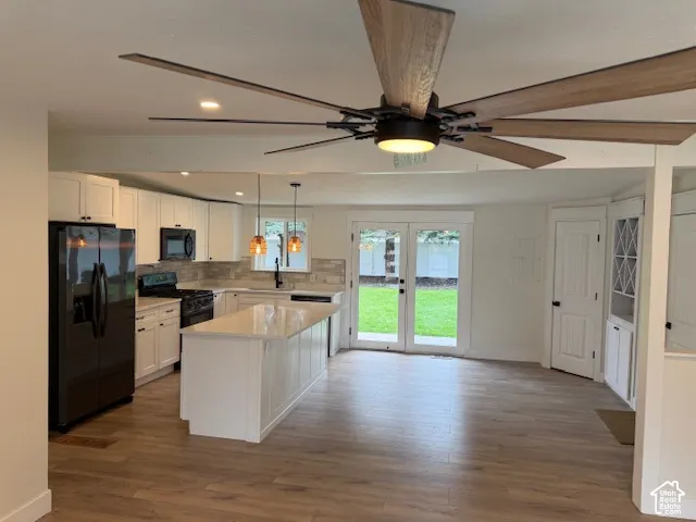 Kitchen featuring a central island with a solid surface countertop, white cabinetry, dark-finish appliances, wood-finish flooring, and a multi-blade ceiling fan with integrated lighting