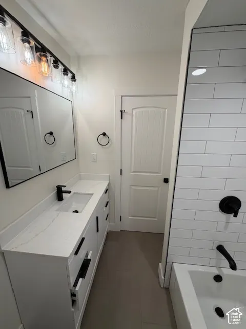 Bathroom vanity with stone-look countertop, integrated rectangular sink, matte black hardware, linear light fixture, and subway-tiled shower surround