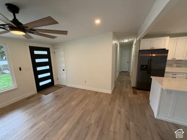 Wood-finish flooring, multi-panel front door with frosted glass inserts, matte black ceiling fan, white shaker-style cabinetry, and stone-finish countertops