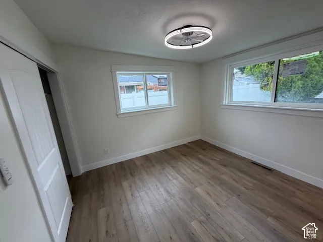 Room featuring wood-finish flooring, two windows with white trim, a sliding panel door, and a circular LED flush-mount fixture
