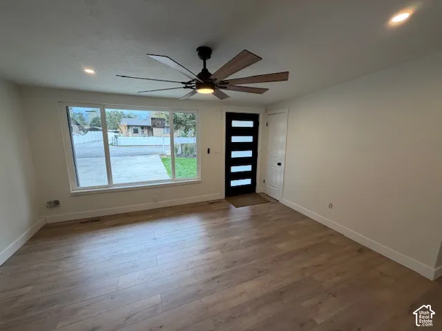 Room featuring wood-finish flooring, a multi-pane picture window, modern ceiling fan with integrated lighting, and a six-panel glass-inset entry door