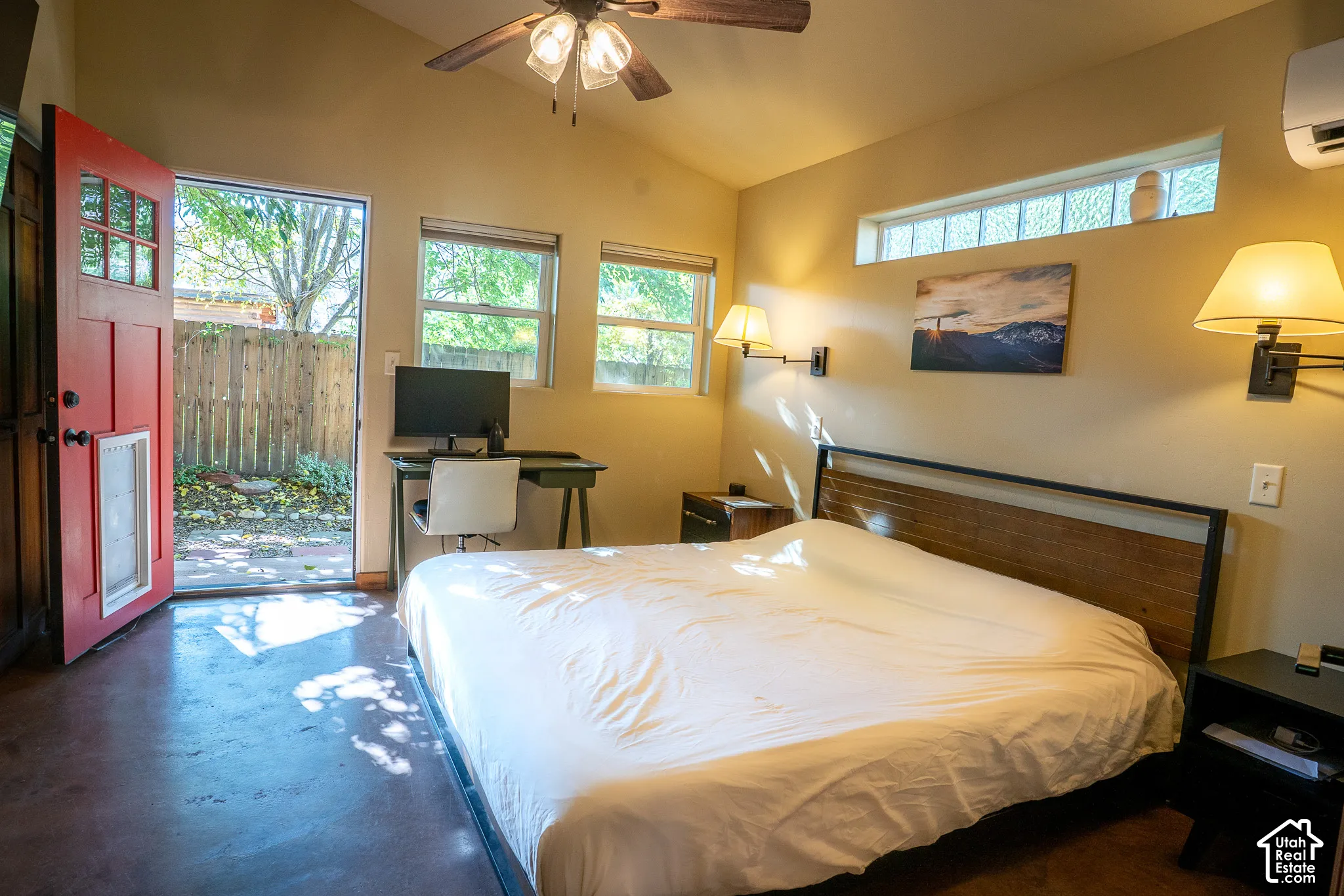 Vaulted ceiling with a central ceiling fan, stained concrete flooring, horizontal transom window, and exterior door with a multi-pane glass insert