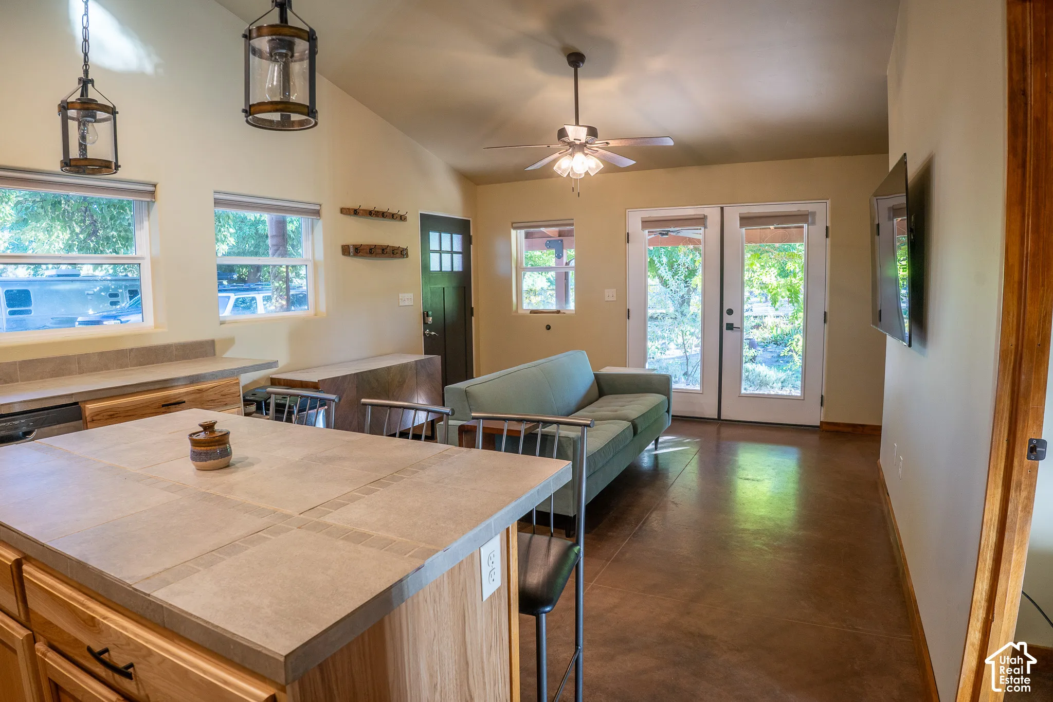 Open-concept living space featuring stained concrete flooring, vaulted ceilings, a kitchen island with tile surfacing, pendant lighting, and double glass-panel entry doors