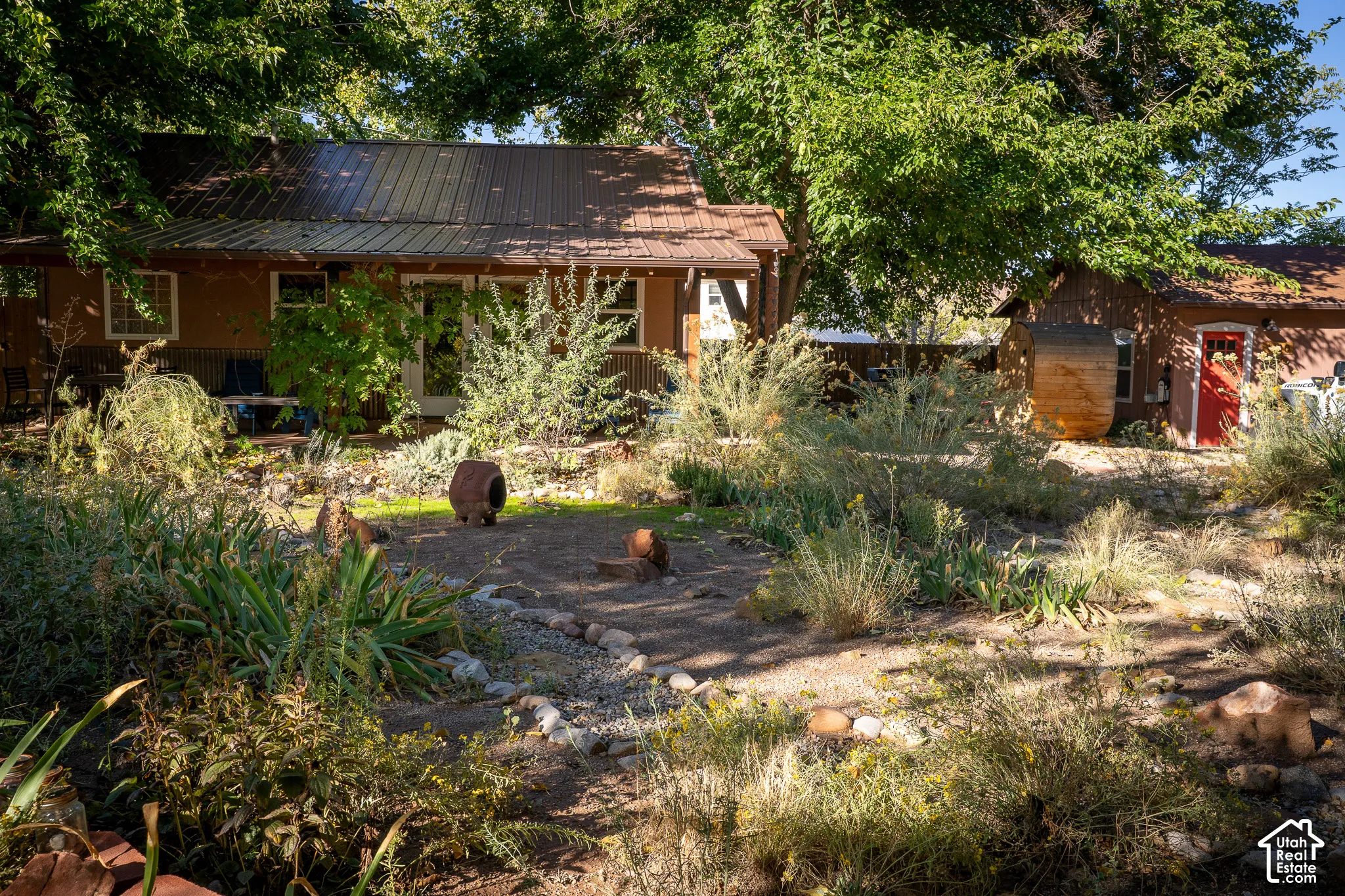 Xeriscape backyard featuring native plantings, rock garden elements, metal roofing, and a barrel-style structure