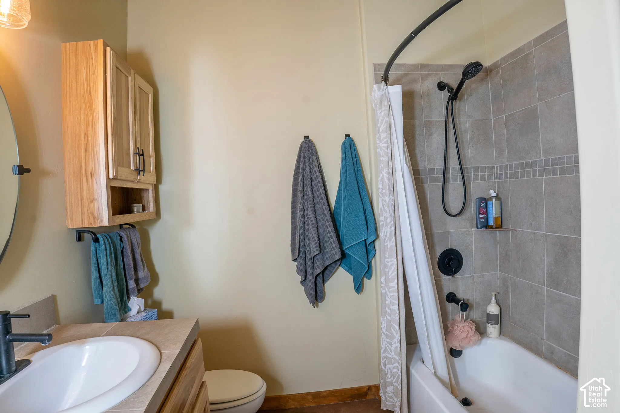 Bathroom featuring a vanity with tile countertop, wall-mounted wood cabinetry, and a shower-tub combination with stone-tile surround and matte black fixtures