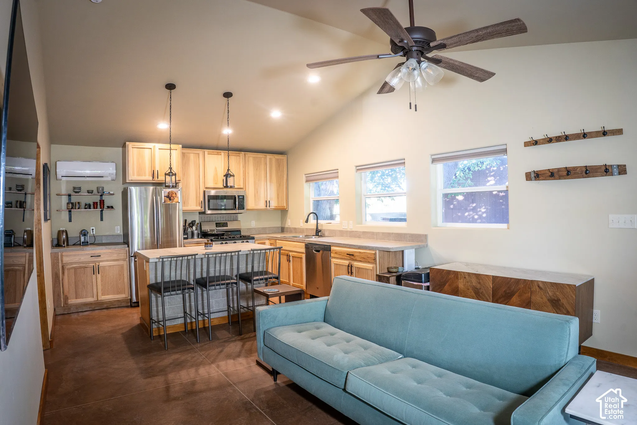 Open-concept kitchen featuring light wood cabinetry, stone countertops, stainless steel appliances, dual pendant lighting, and vaulted ceilings