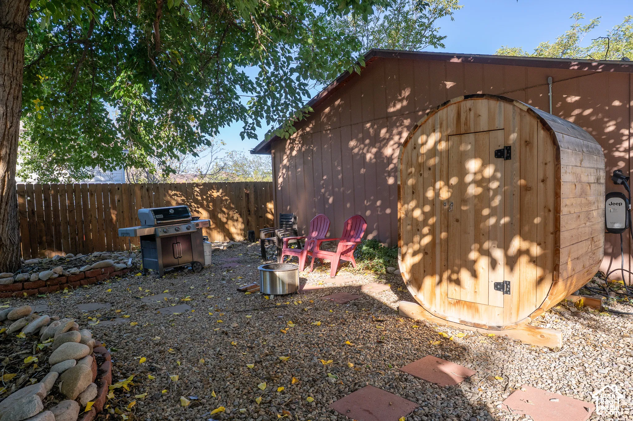 Outdoor space featuring a barrel sauna, gravel ground cover, a tiered river-rock garden bed, and wood-paneled exterior siding