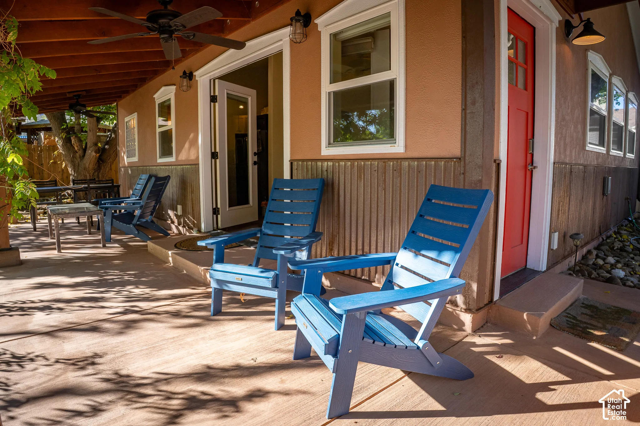 Covered patio featuring a concrete floor, corrugated metal wainscoting, a wood-beam ceiling with an integrated fan, and exterior wall-mounted lighting