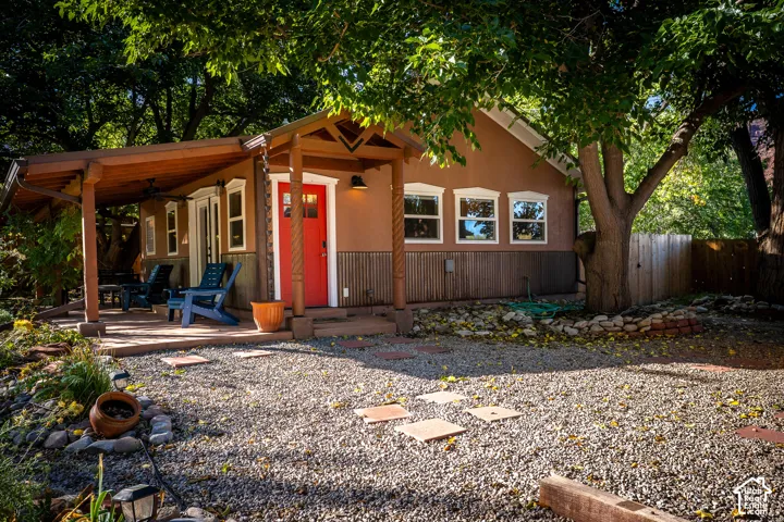 Exterior featuring a covered patio, metal wainscoting, decorative wood-turned posts, and a vibrant red entry door, complemented by a gravel yard