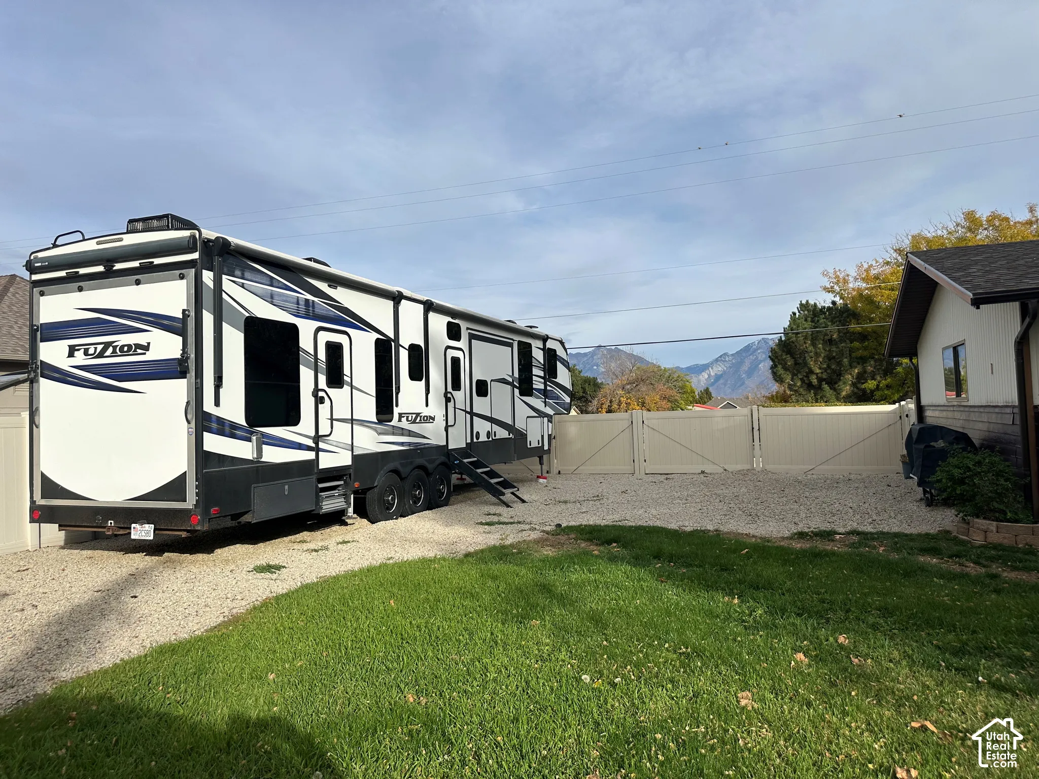 Gravel parking area enclosed by a solid vinyl privacy fence, featuring a manicured lawn and mountain scenery