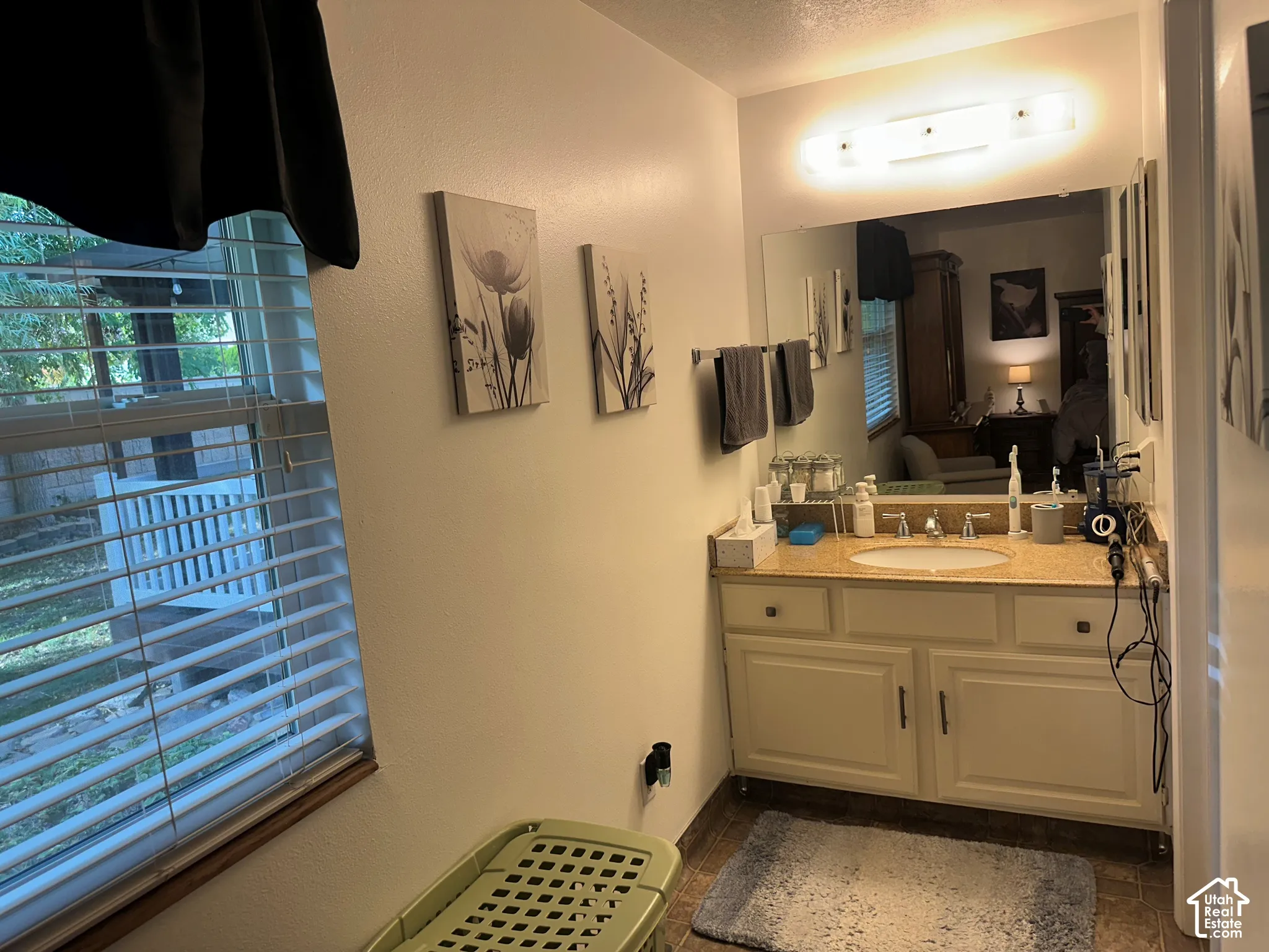 Vanity featuring a stone-composite countertop, oval undermount sink, multi-drawer cabinetry, full-width mirror, and multi-bulb wall-mounted lighting