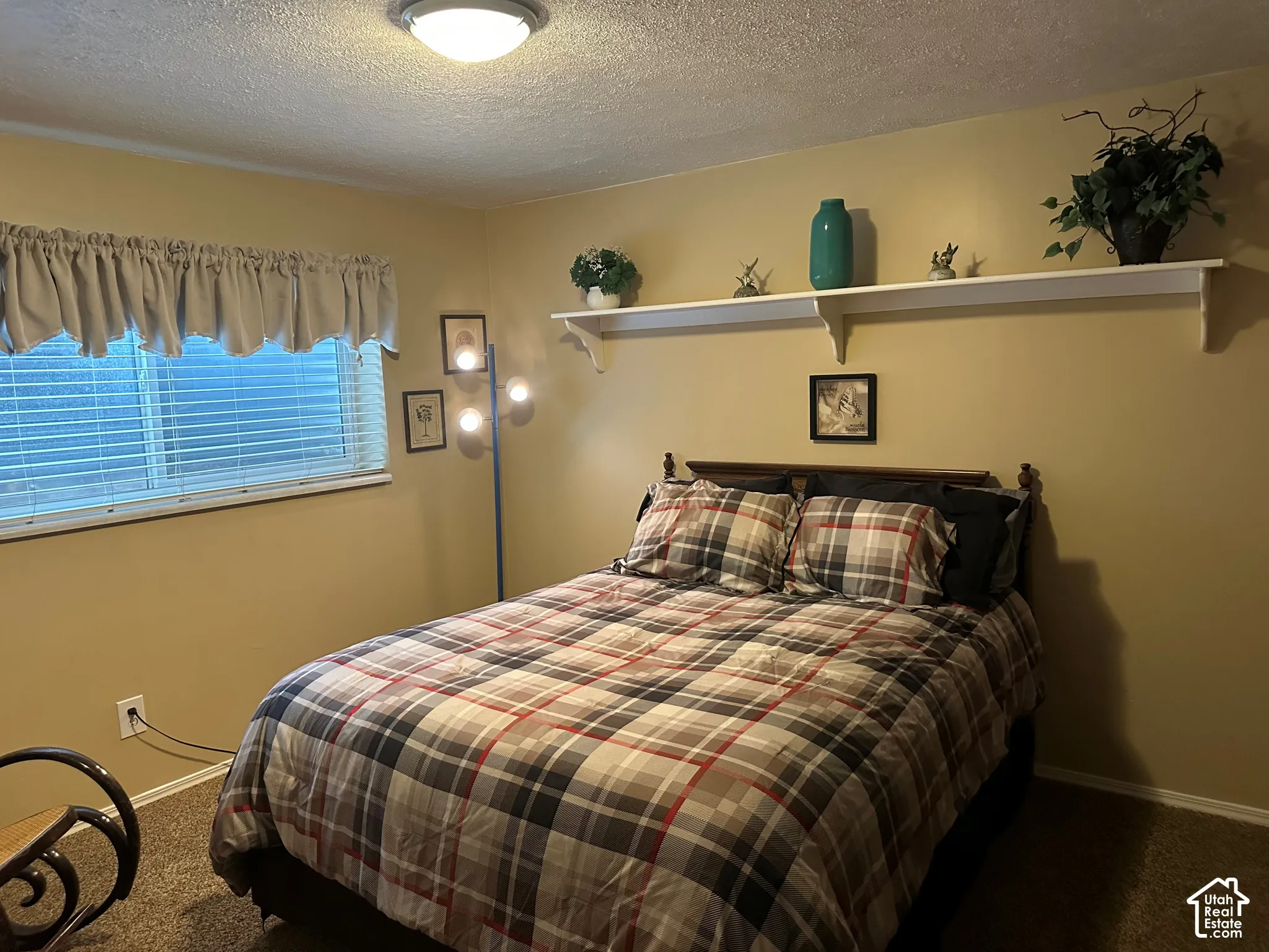 Neutral-toned room featuring textured ceilings, carpeted flooring, a horizontal sliding window, and a built-in wall-mounted shelving unit