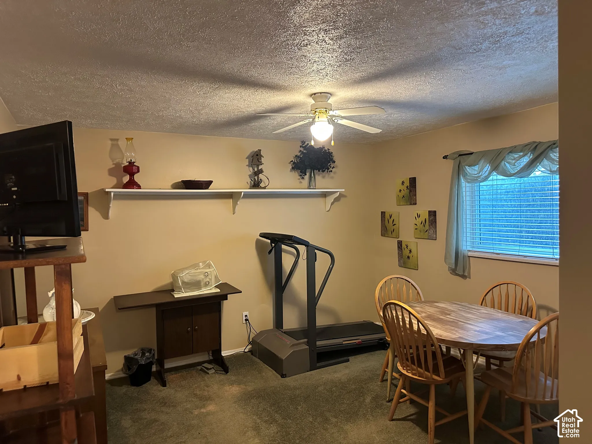 Room featuring a textured ceiling, a mounted white wall shelf, and a center-mount ceiling fan