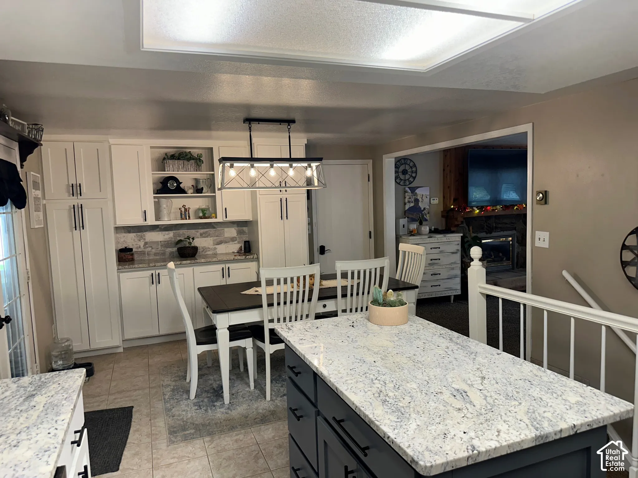 Kitchen featuring a central island with a stone-finish countertop and charcoal cabinetry, white shaker-style perimeter cabinetry, custom built-in pantry storage, a tile backsplash, and overhead pendant lighting