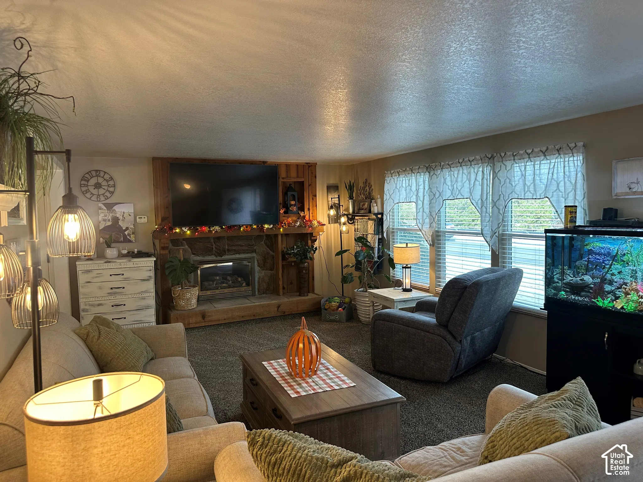 Living area featuring a floor-to-ceiling stone fireplace, natural wood built-in shelving, carpeted flooring, and oversized windows
