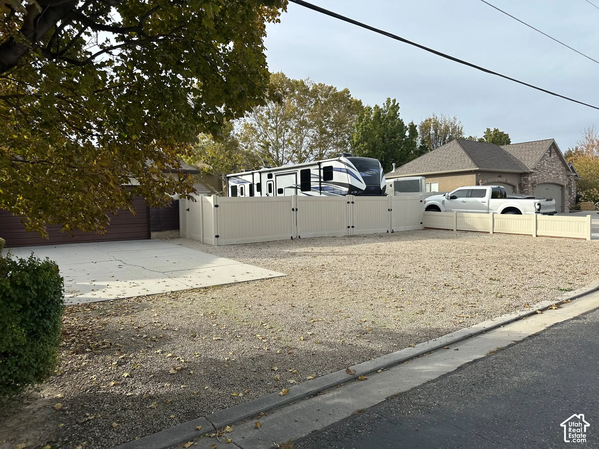 Expansive gravel parking area featuring concrete driveway sections and white vinyl privacy fencing