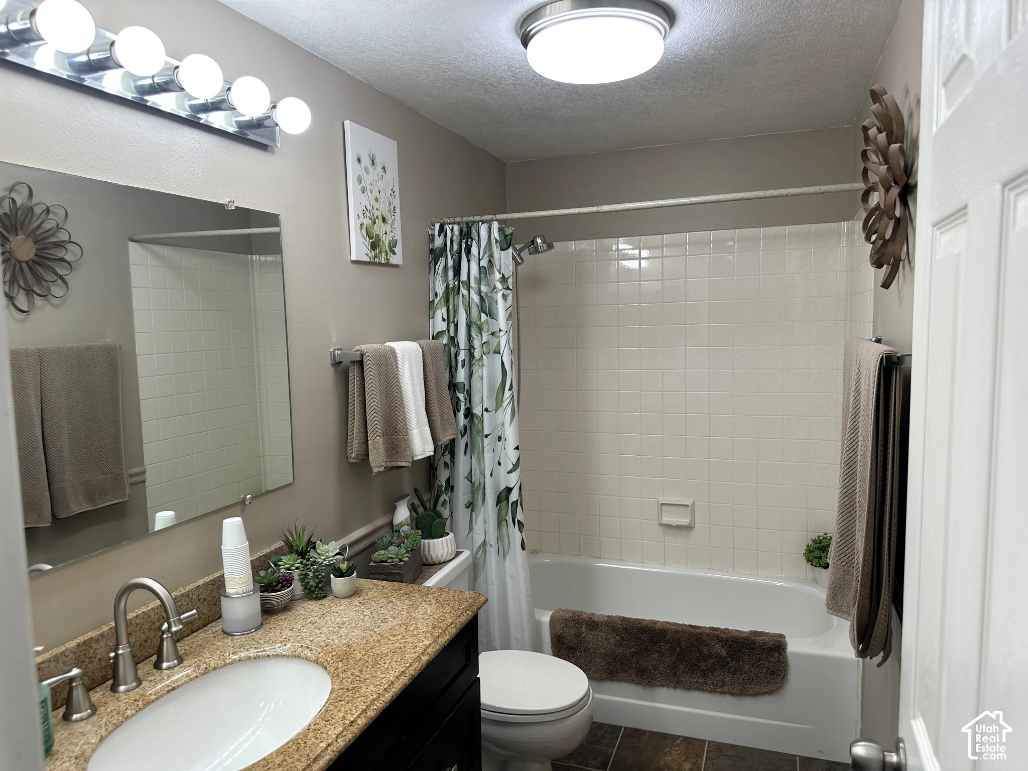 Bathroom featuring a dark wood-finish vanity, stone-surface countertop with an integrated basin, large wall-mounted mirror, and a tub-shower combination with tiled surround
