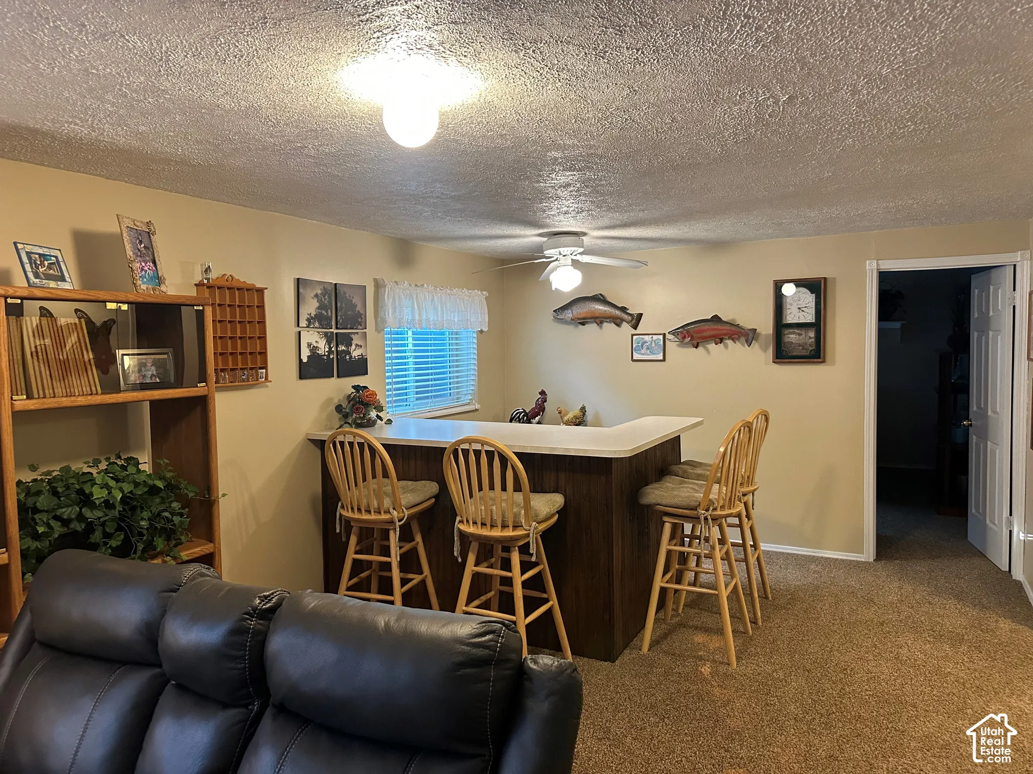 Built-in wooden shelving unit, recessed bar featuring a solid-surface countertop and dark wood-finish cabinetry, and a ceiling-mounted paddle fan