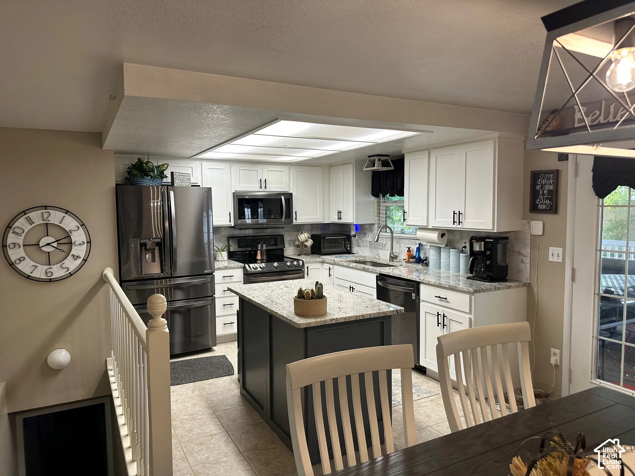 Kitchen featuring white cabinetry with dark hardware, a central island with a contrasting dark finish, speckled stone-composite countertops, stainless steel appliances, and recessed tray lighting