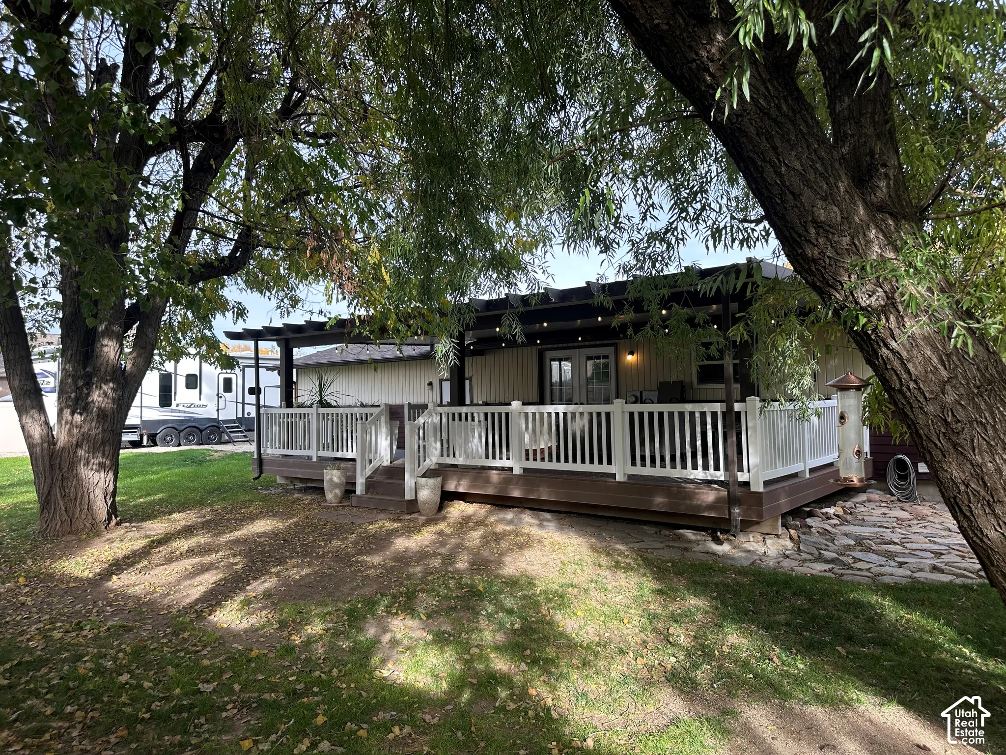 Rear deck featuring a dark composite surface, white railing, built-in pergola, and stone hardscaping