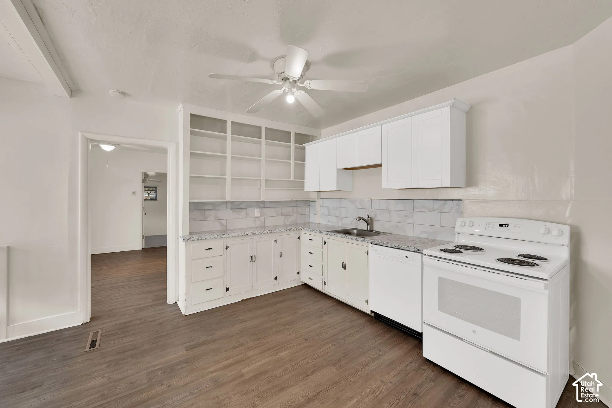 Kitchen featuring white shaker-style cabinetry, floor-to-ceiling built-in shelving, stone-composite countertops, subway tile backsplash, and wood-finish flooring