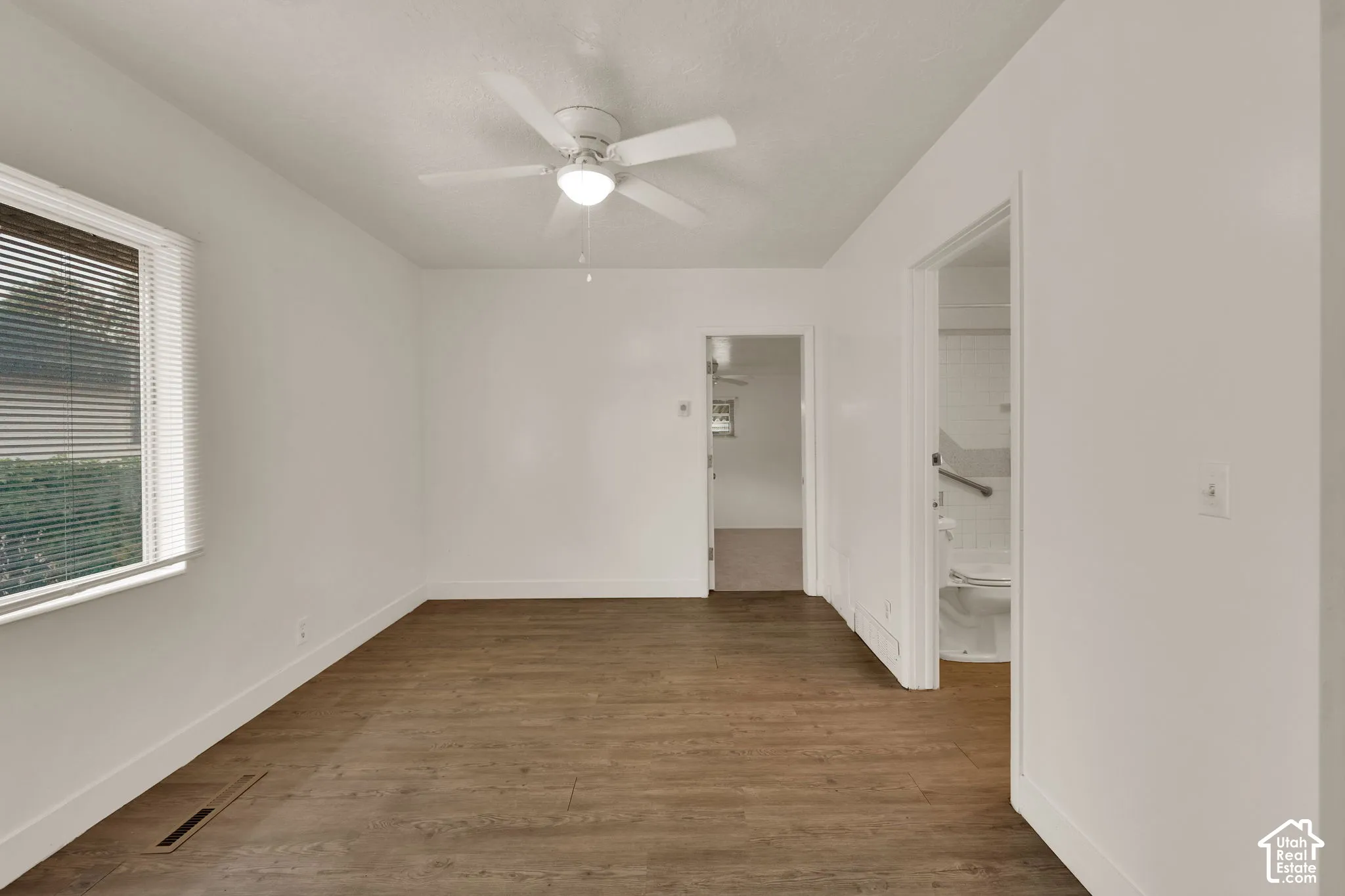 Room featuring wood-finish flooring, white walls, and a ceiling-mounted light fixture with integrated fan