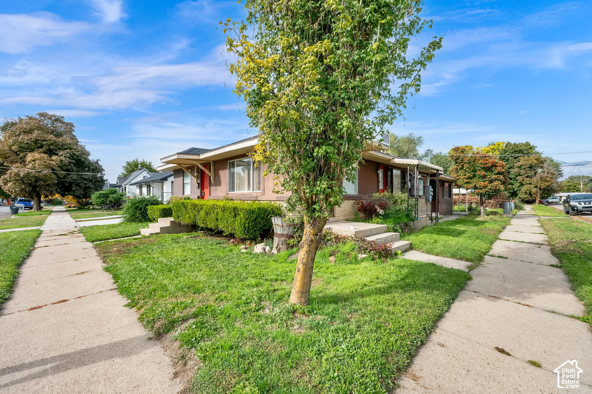 Single-story exterior featuring a brick and stucco facade, concrete porch steps, and mature landscaping