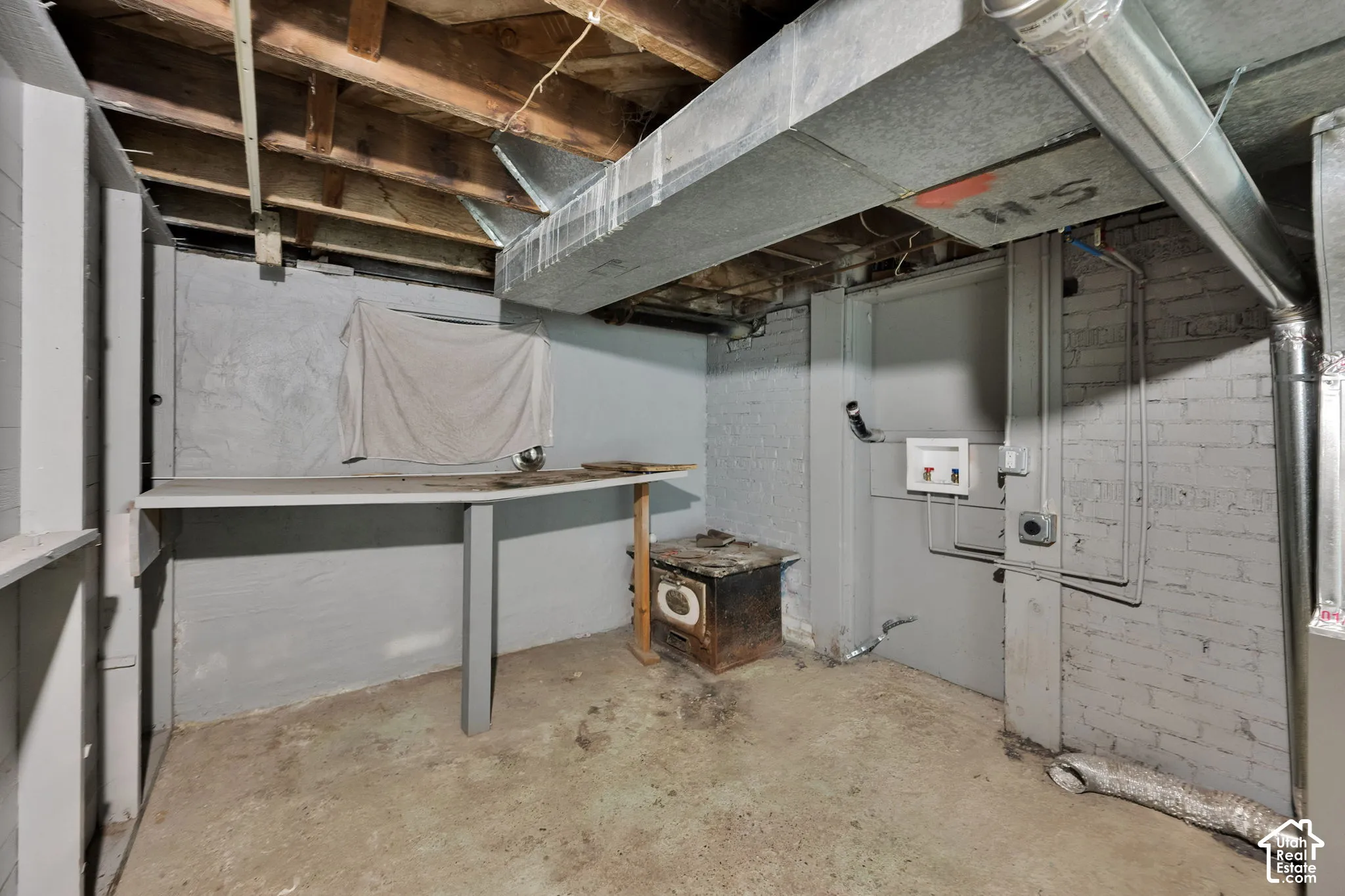 Unfinished utility space featuring painted brick walls, exposed wood ceiling joists, concrete flooring, built-in shelving, and dedicated laundry hookups