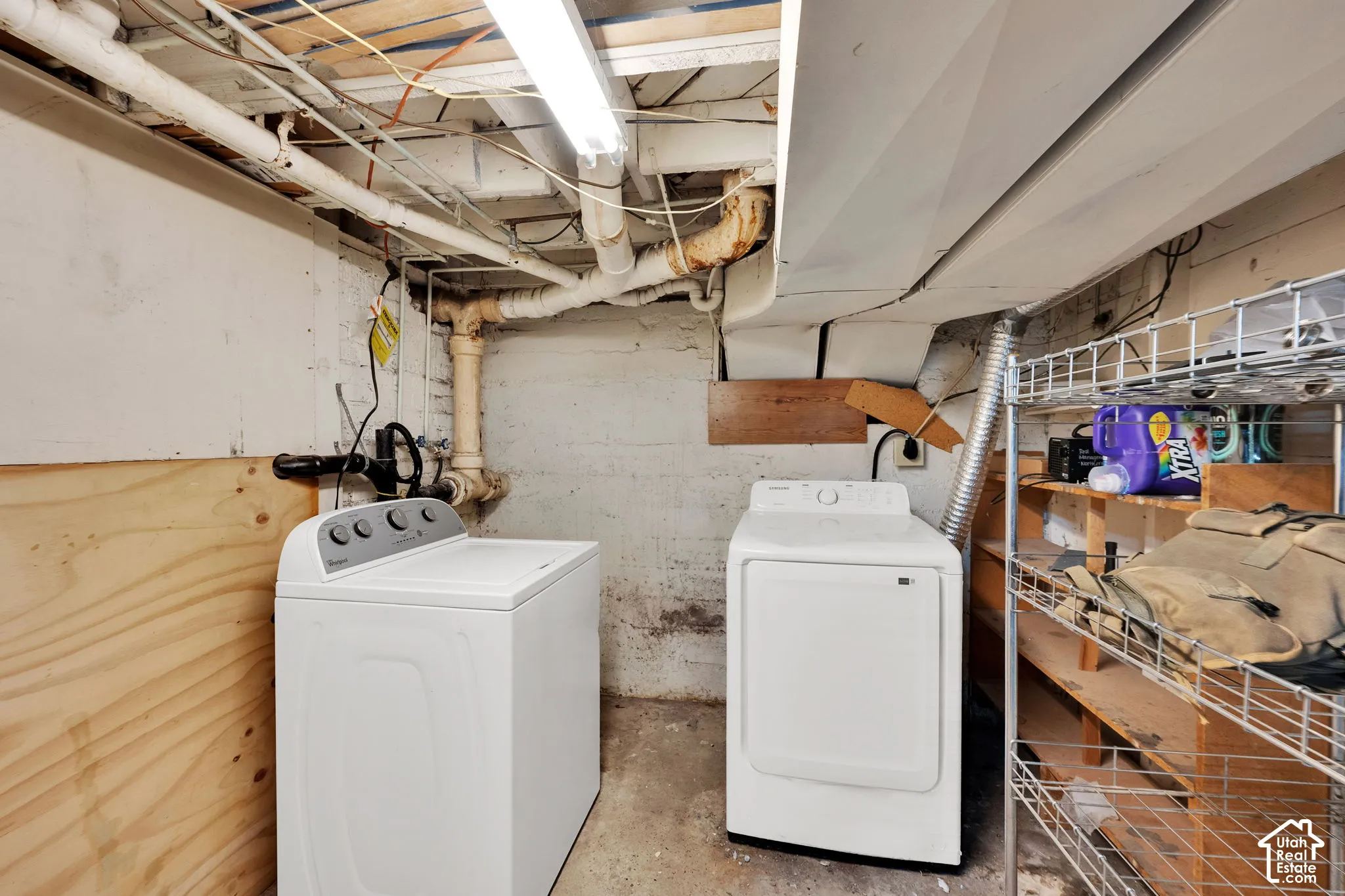 Utility area featuring exposed plumbing, painted masonry walls, plywood paneling, and an overhead fluorescent light fixture