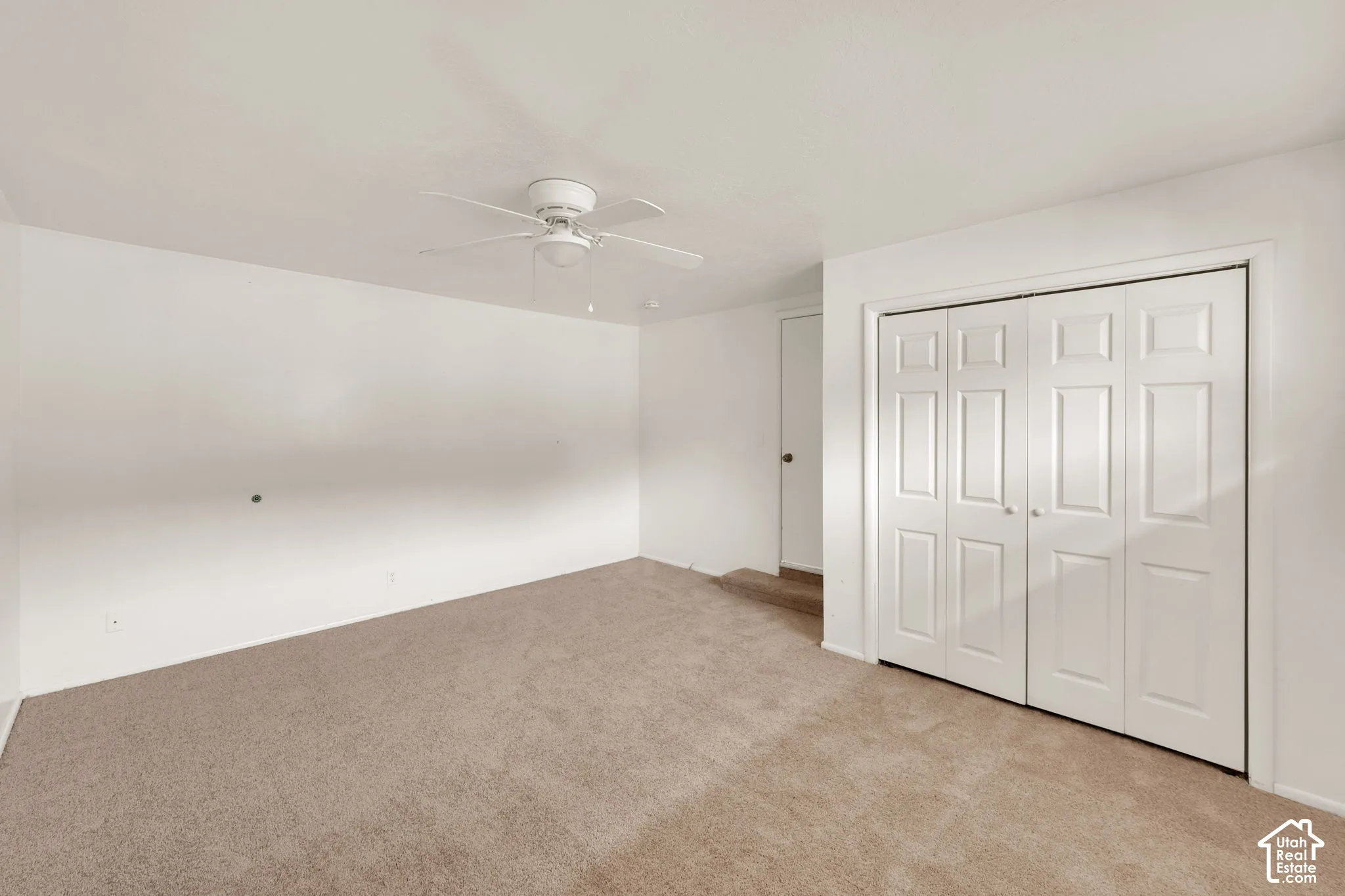 Interior room featuring neutral carpeting, a ceiling fan with integrated lighting, and a closet with white bifold doors