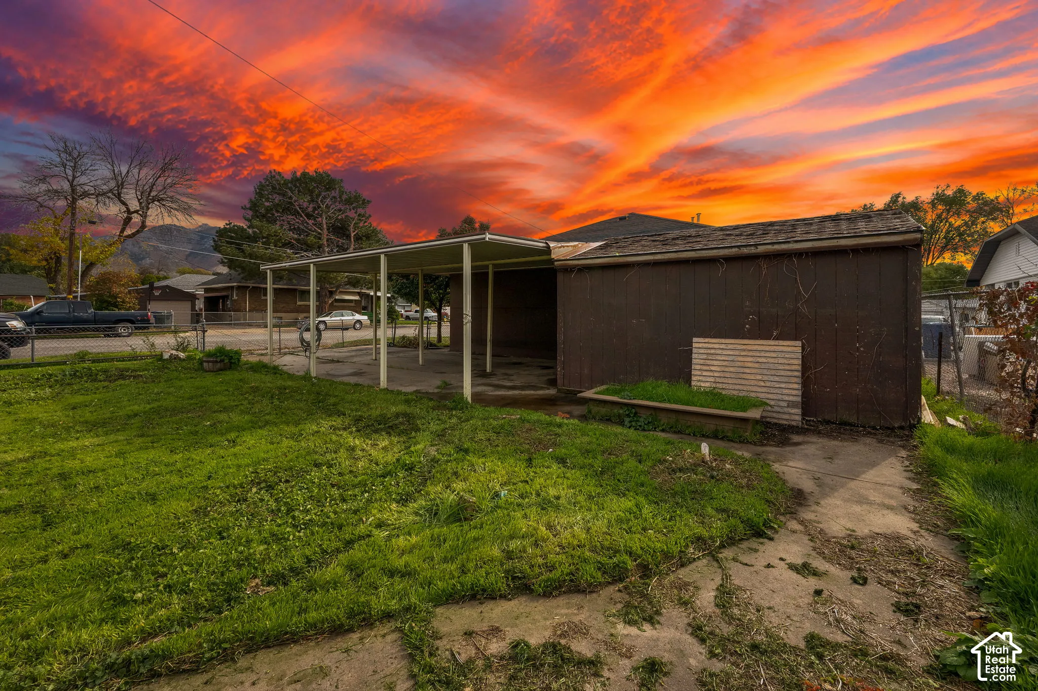 Exterior features including a covered carport, wood-panel siding, concrete surfacing, and a fenced yard