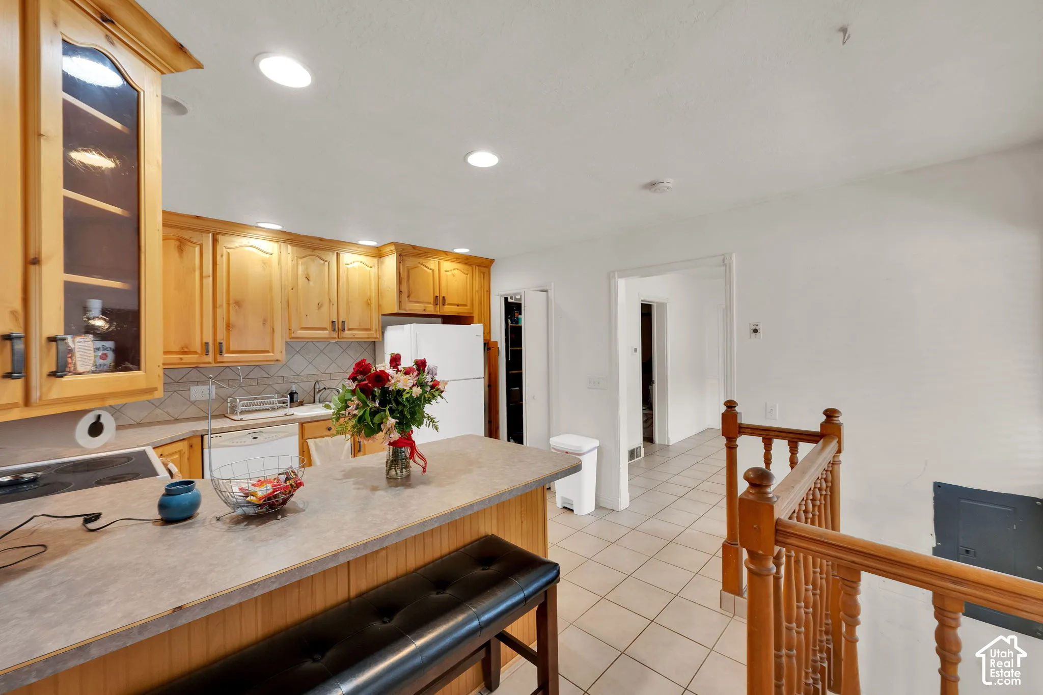 Kitchen featuring natural wood cabinetry, solid surface countertop, tile backsplash, and ceramic tile flooring, complemented by a wooden banister
