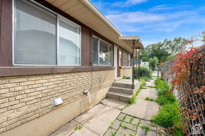 Exterior elevation featuring a tan brick facade, painted horizontal siding, metal-frame windows, and a concrete pathway leading to a raised entry with a metal-supported awning