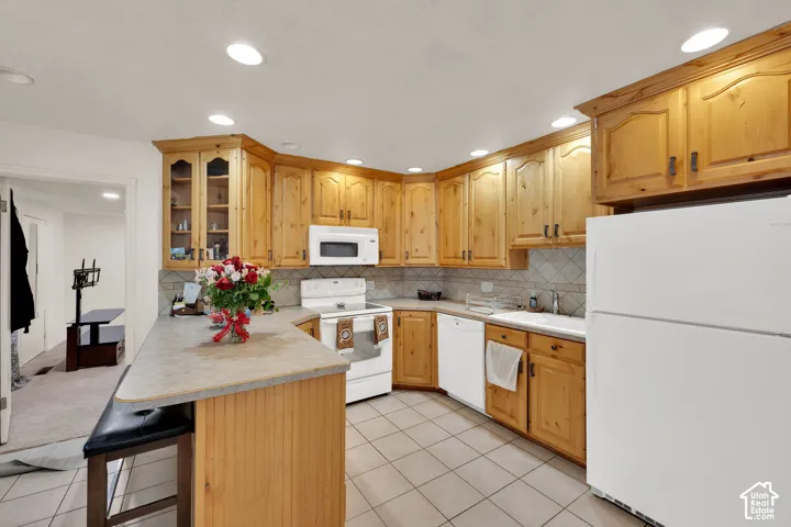 Kitchen featuring natural wood cabinetry, peninsula with bar seating, tiled flooring, built-in microwave, and recessed lighting