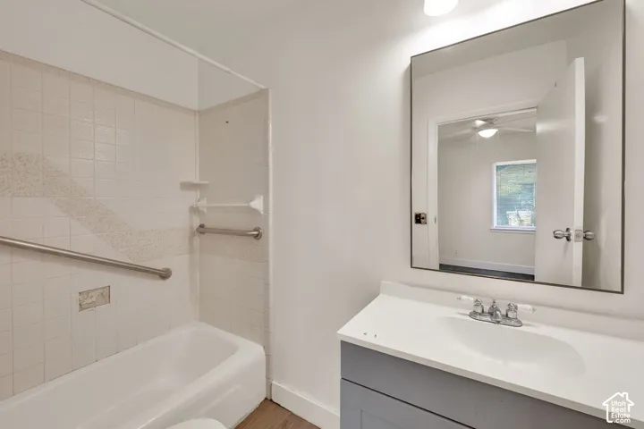 Bathroom featuring a vanity with a white countertop and integrated sink, a large wall-mounted rectangular mirror, and a tub-shower combination with tiled surround and metal grab bars