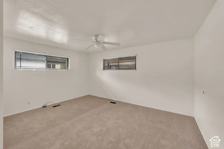 Neutral-toned carpeting, white walls, dual horizontal sliding windows, and a ceiling-mounted light fixture with a fan